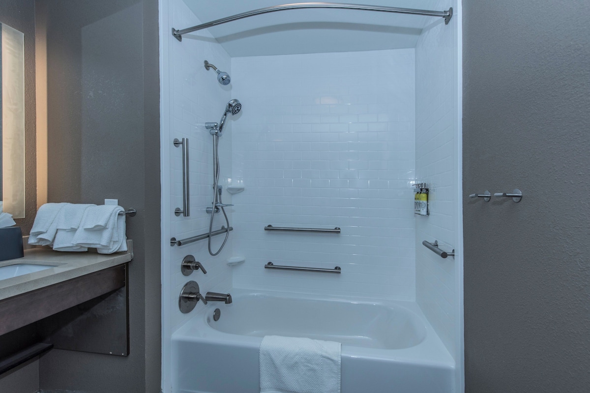 A modern bathroom with a bathtub, shower, and toilet. It includes a towel rack, a soap dispenser, and a hand dryer.