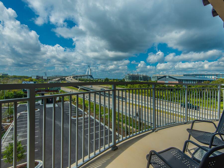 A balcony with a view of a parking lot, a bridge, and modern buildings.