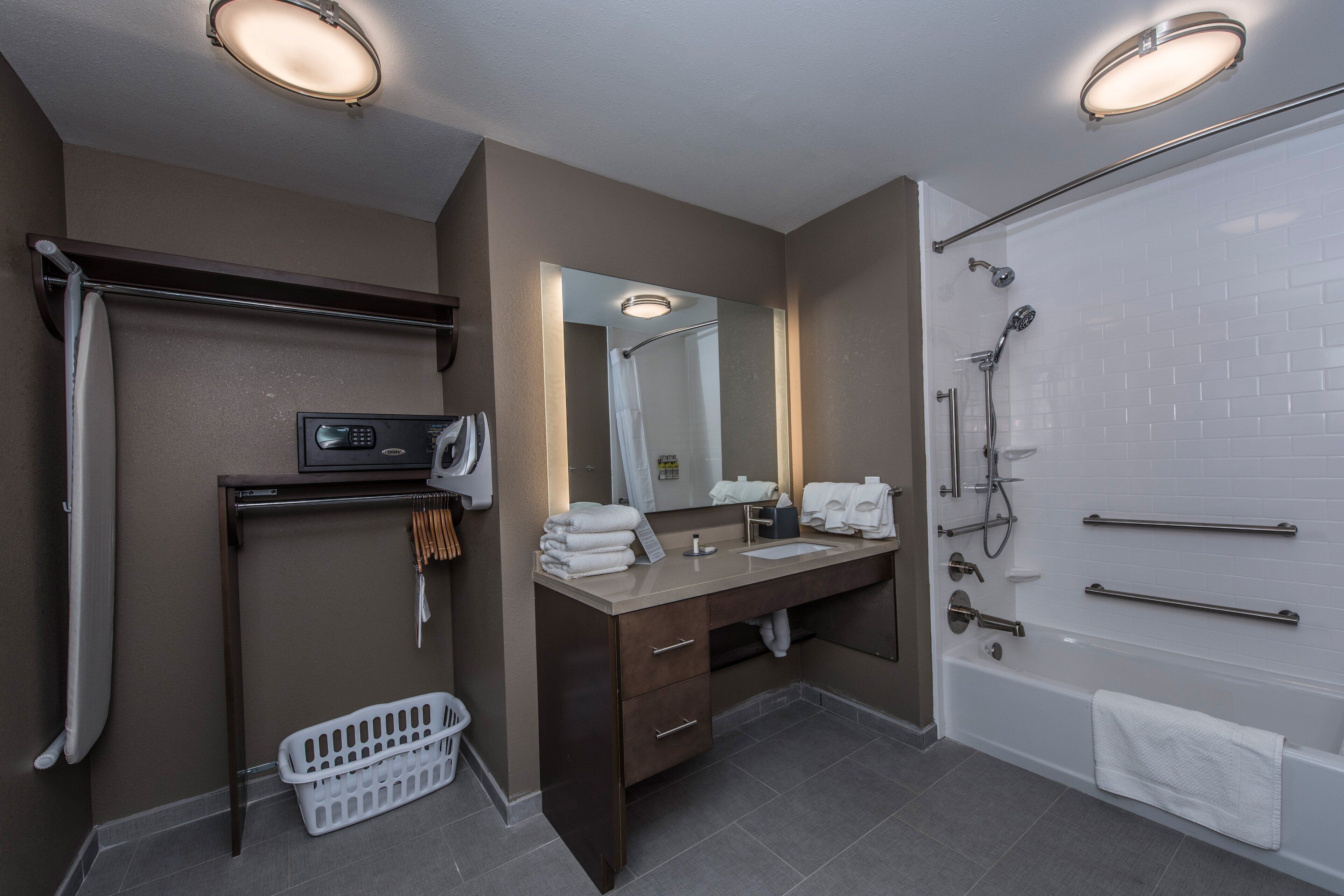 Une salle de bain moderne équipée d’une douche, d’un meuble-lavabo avec miroir et d’un panier à linge.