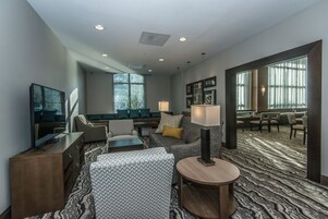 A modern hotel lobby with a seating area, a television, and a patterned carpet.