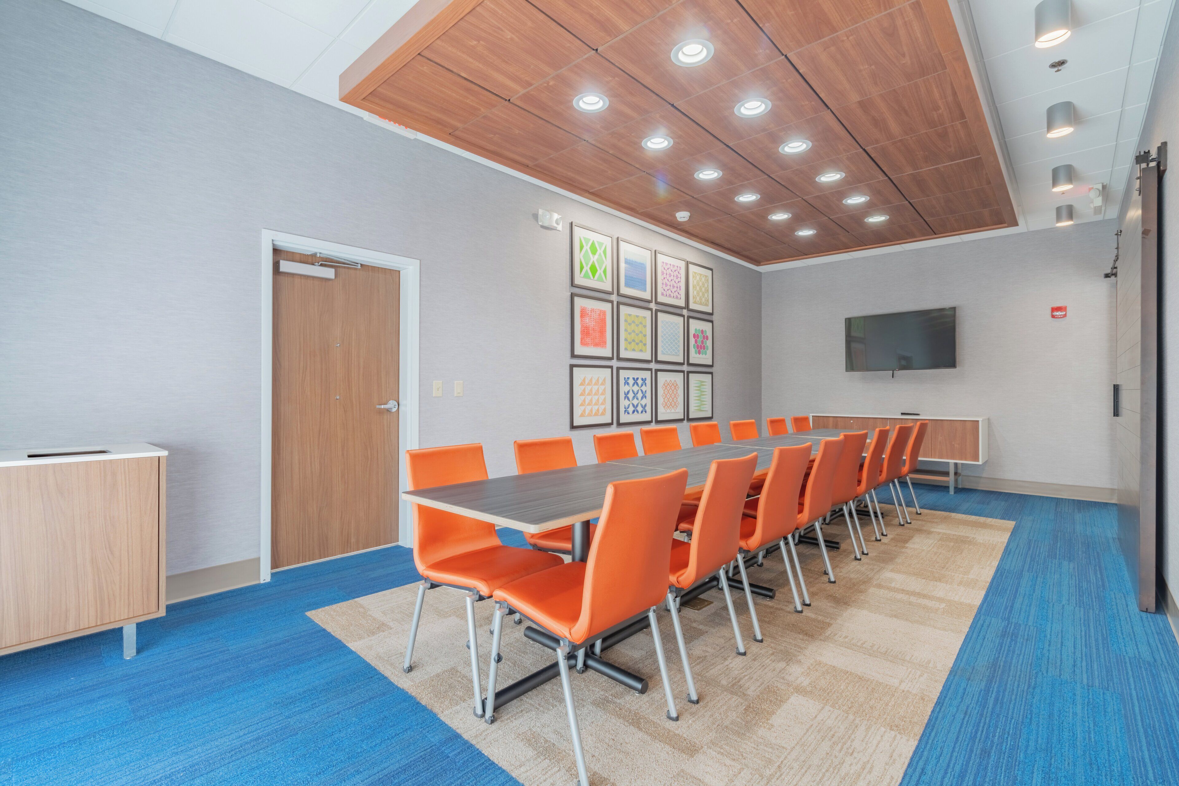 A conference room with a long table, orange chairs, a wooden ceiling, and a blue carpet.