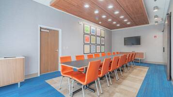 Una sala conferenze con un lungo tavolo, sedie arancioni, soffitto in legno e tappeto blu.