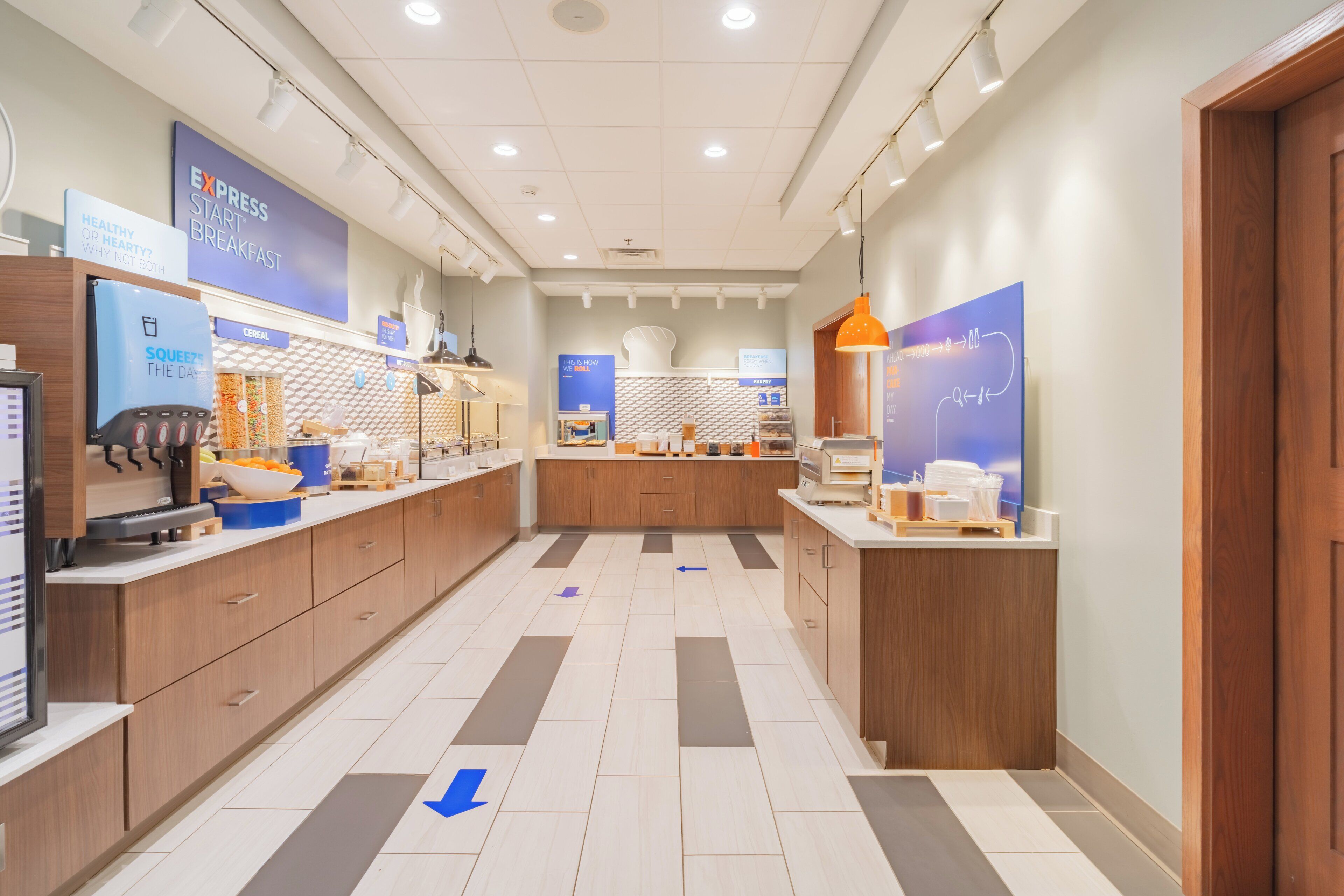 A modern hotel lobby with a central counter, wooden cabinets, and directional arrows on the floor.
