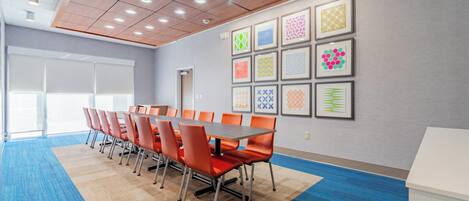 Une salle de conférence avec une longue table, des chaises orange, une moquette bleue et des œuvres d’art encadrées accrochées au mur.