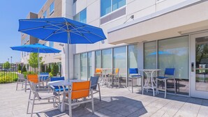 An outdoor patio area with tables and chairs, blue umbrellas, and a modern building with large windows. - Holiday Inn Express & Suites Marion by IHG (Marion)