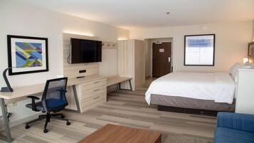 A hotel room with a bed, a desk with a chair, a television, and a framed picture on the wall.