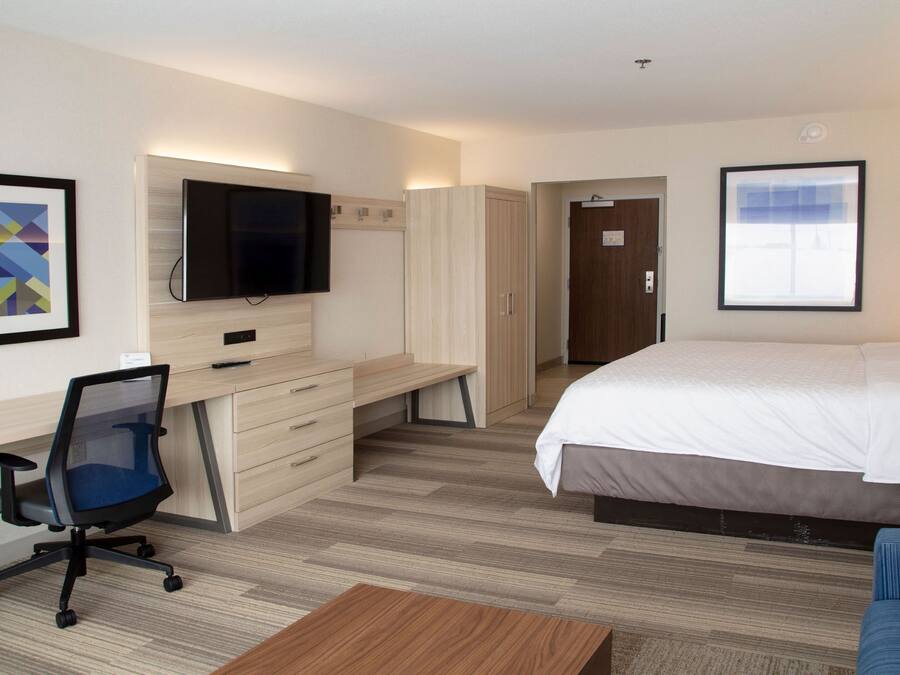A hotel room with a bed, a desk with a chair, a television, and a framed picture on the wall.