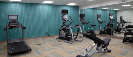 Une salle de sport équipée de tapis de course, de vélos elliptiques et d’un banc de musculation.