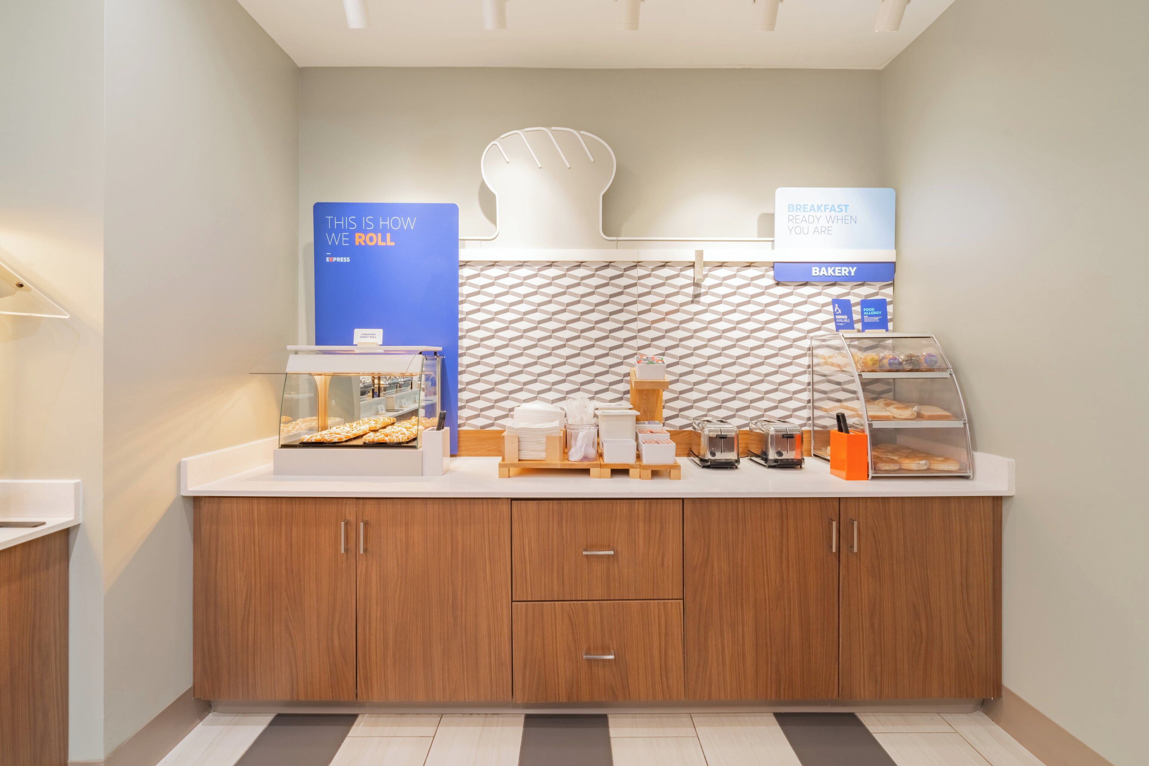 Un comptoir de petit-déjeuner moderne, agrémenté d’un pare-feu géométrique, d’un présentoir à pain et d’un panneau indiquant que le petit-déjeuner est servi.