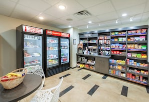 A snack shop with shelves stocked with various snacks and a refrigerator with beverages. - Candlewood Suites Houston - Pasadena by IHG (Pasadena)