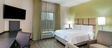 A hotel room with a bed, a desk, a chair, a TV, and a window with curtains.