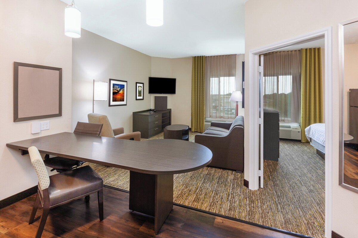 A hotel room with a dining area, a TV, a bed, and a view of the outdoors.