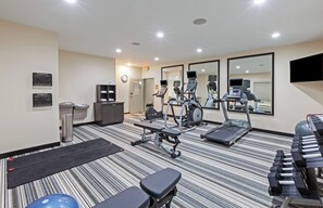 Una sala de gimnàstica d'hotel amb equipament d'exercici, un mirall i un rellotge a la paret.