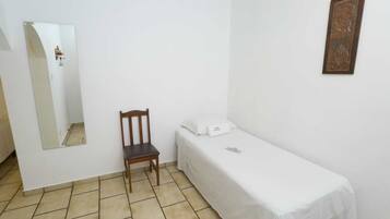 A small, clean room with a single bed, a chair, a bedside table, and a wall-mounted mirror.