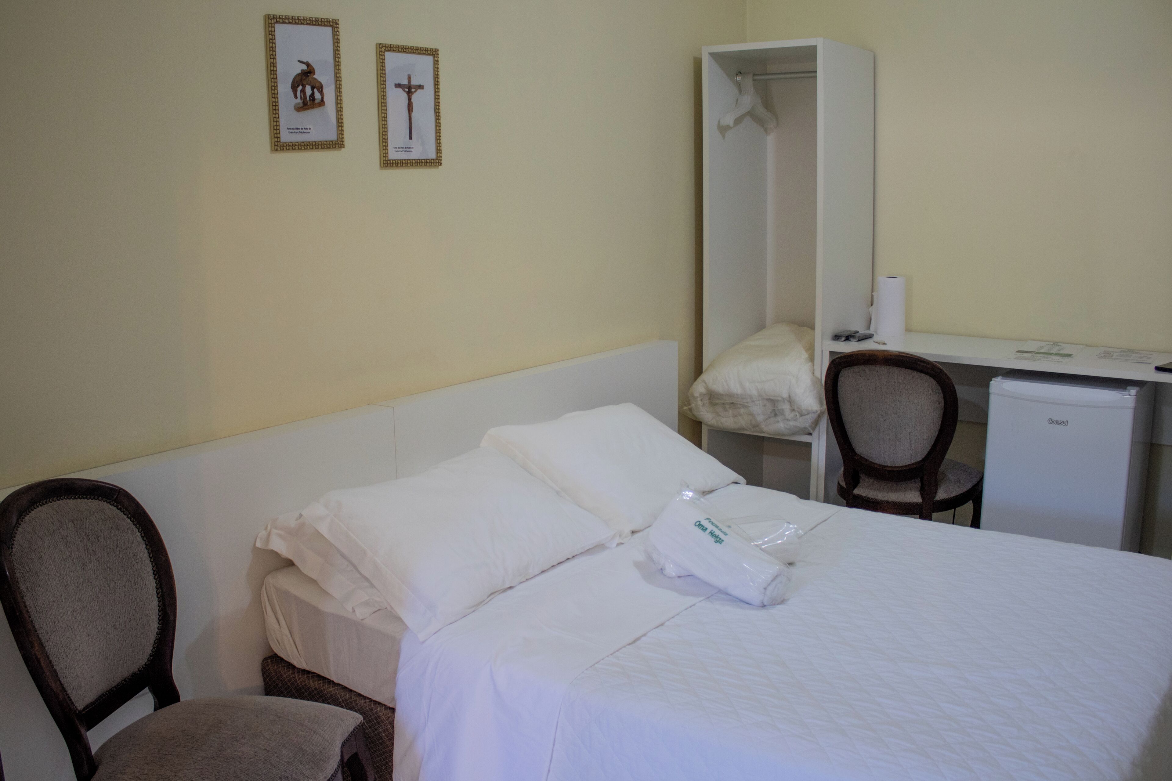 Una habitación de hotel con cama, una silla, un escritorio y un armario.