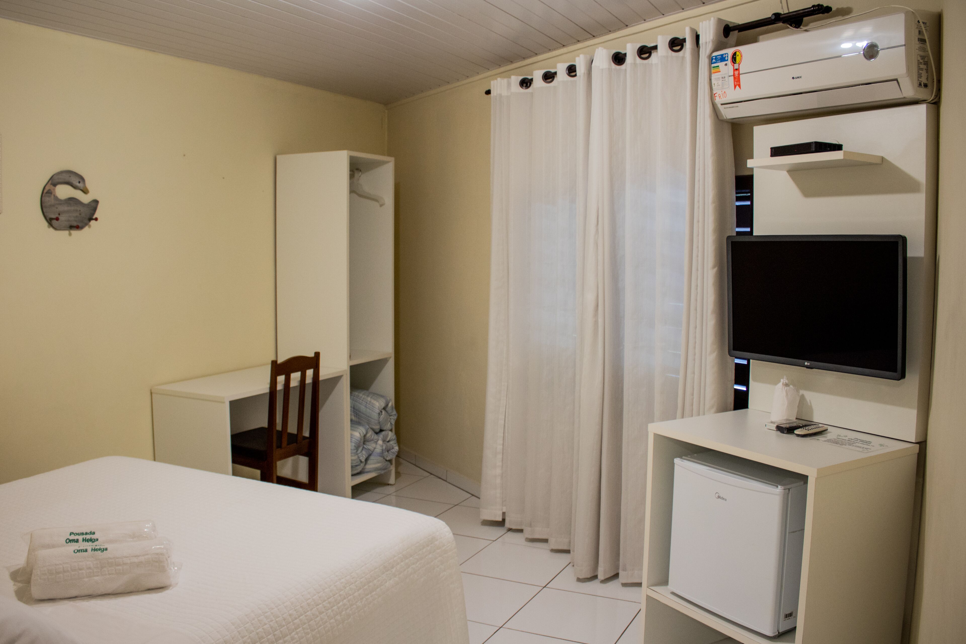 A hotel room with a bed, a desk, a chair, a television, a small refrigerator, and a wardrobe.
