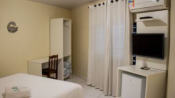 A hotel room with a bed, a desk, a chair, a television, a small refrigerator, and a wardrobe.