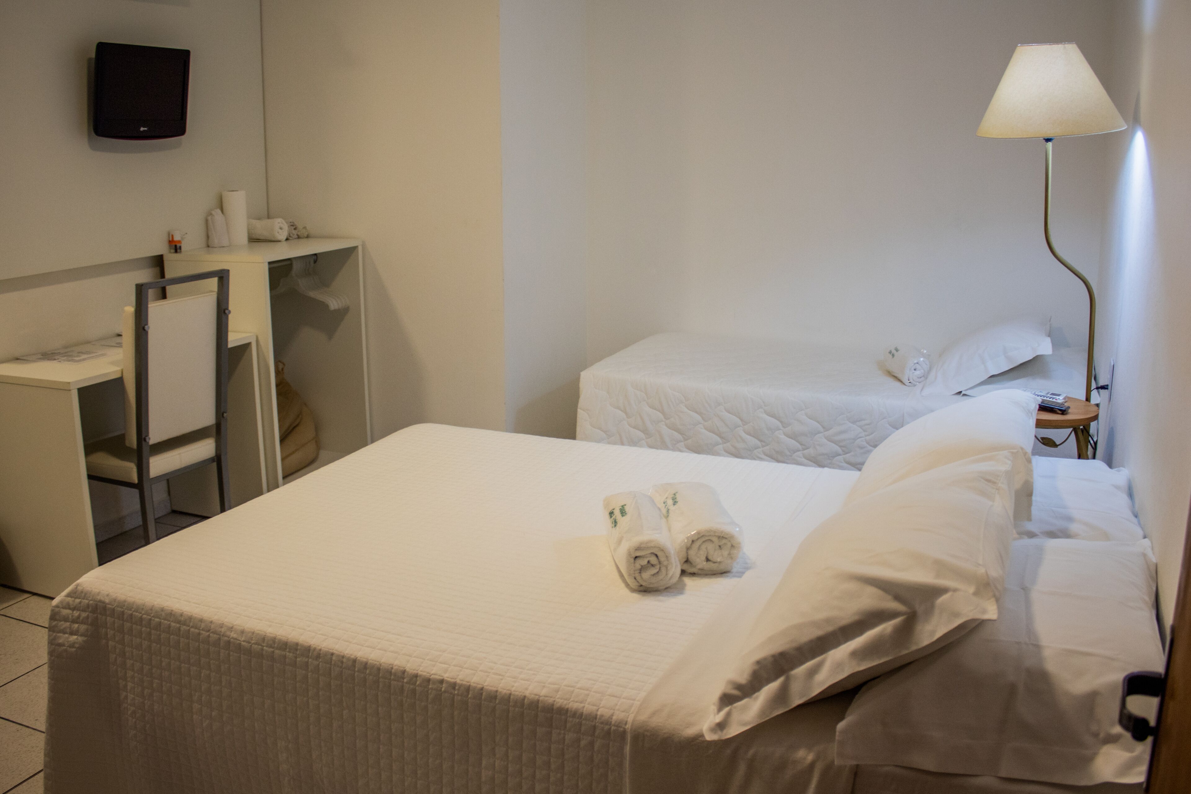 A hotel room with a bed, a desk, a chair, a TV, and a lamp.