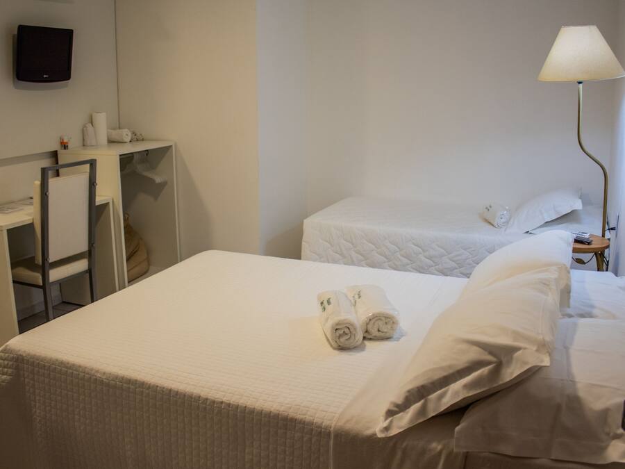 Una habitación de hotel con cama, escritorio, silla, televisor y lámpara.