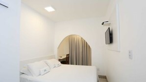 A hotel room with a bed, a TV mounted on the wall, and a small desk with a chair.