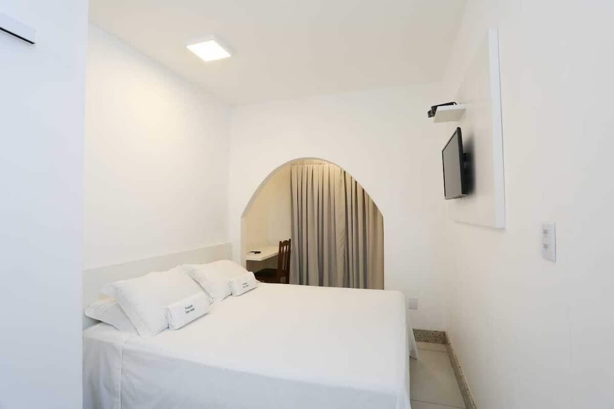 Una habitación de hotel con una cama, un televisor montado en la pared y un pequeño escritorio con una silla.