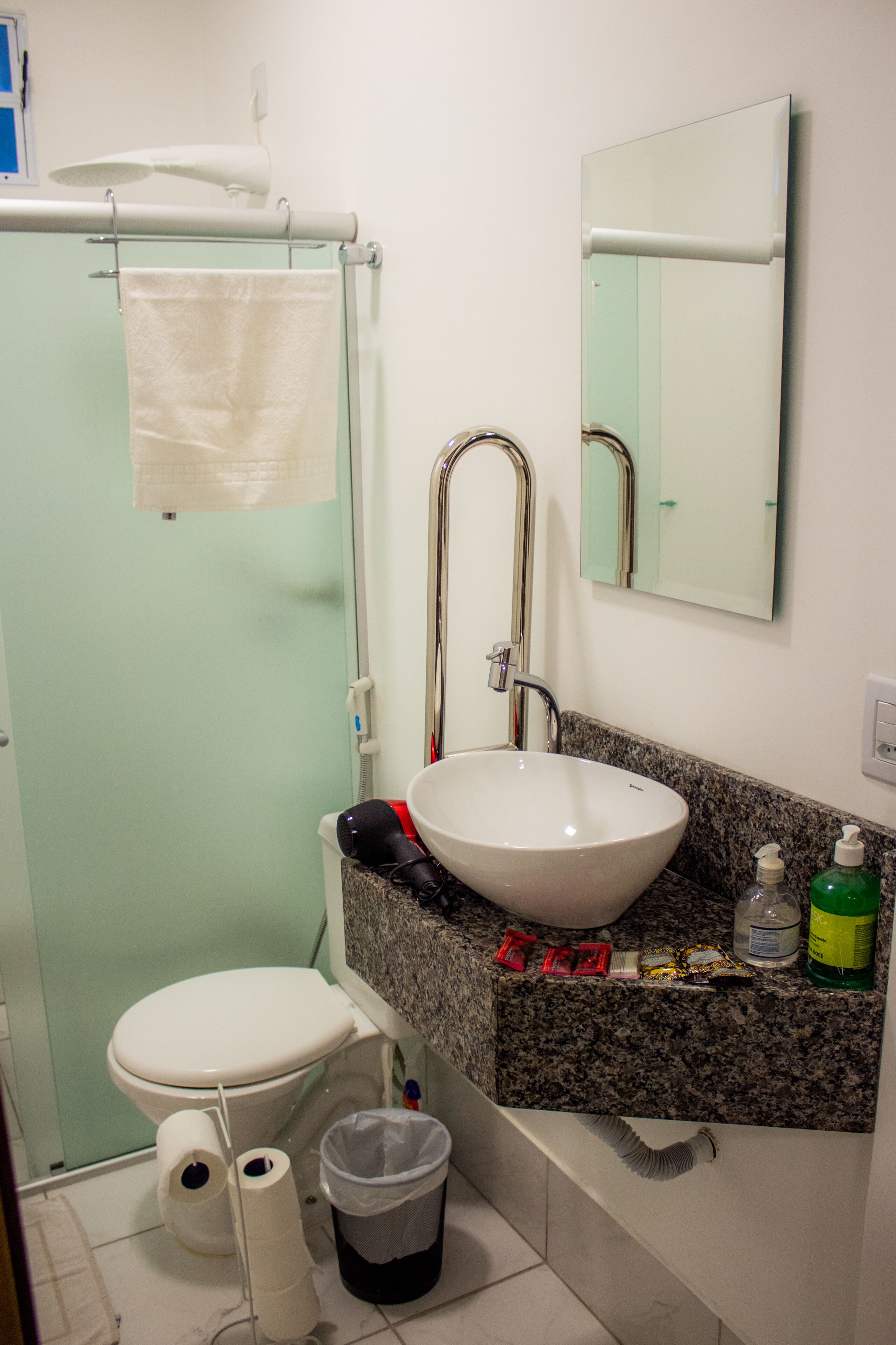 A bathroom with a white sink, a mirror, a towel hanging on a rack, and a trash bin.