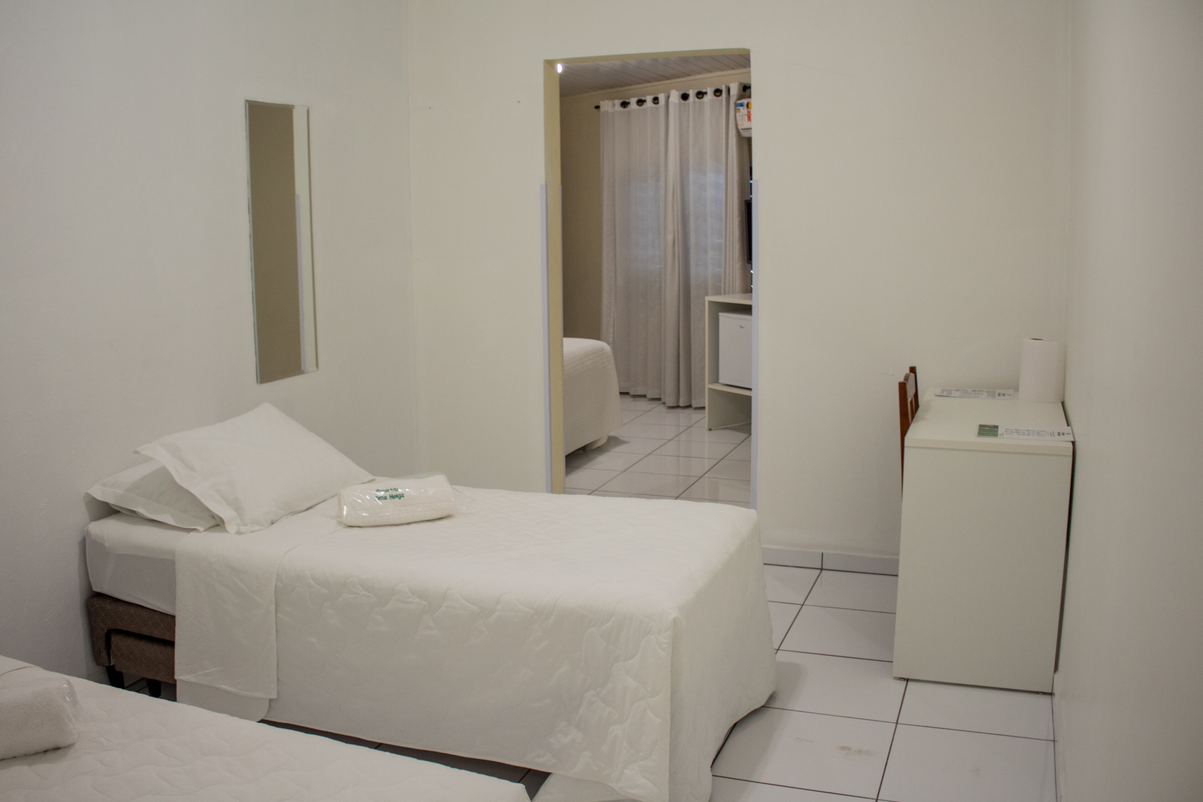 A hotel room with a bed, a small desk, a mirror, and a bathroom visible through an open door.