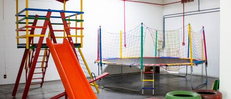 A gymnasium with a climbing structure, a trampoline, and stacked tires.