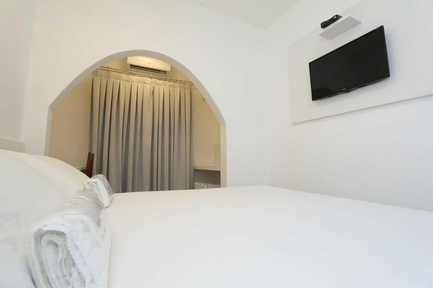 A hotel room with a bed, a TV mounted on the wall, and an arched doorway.