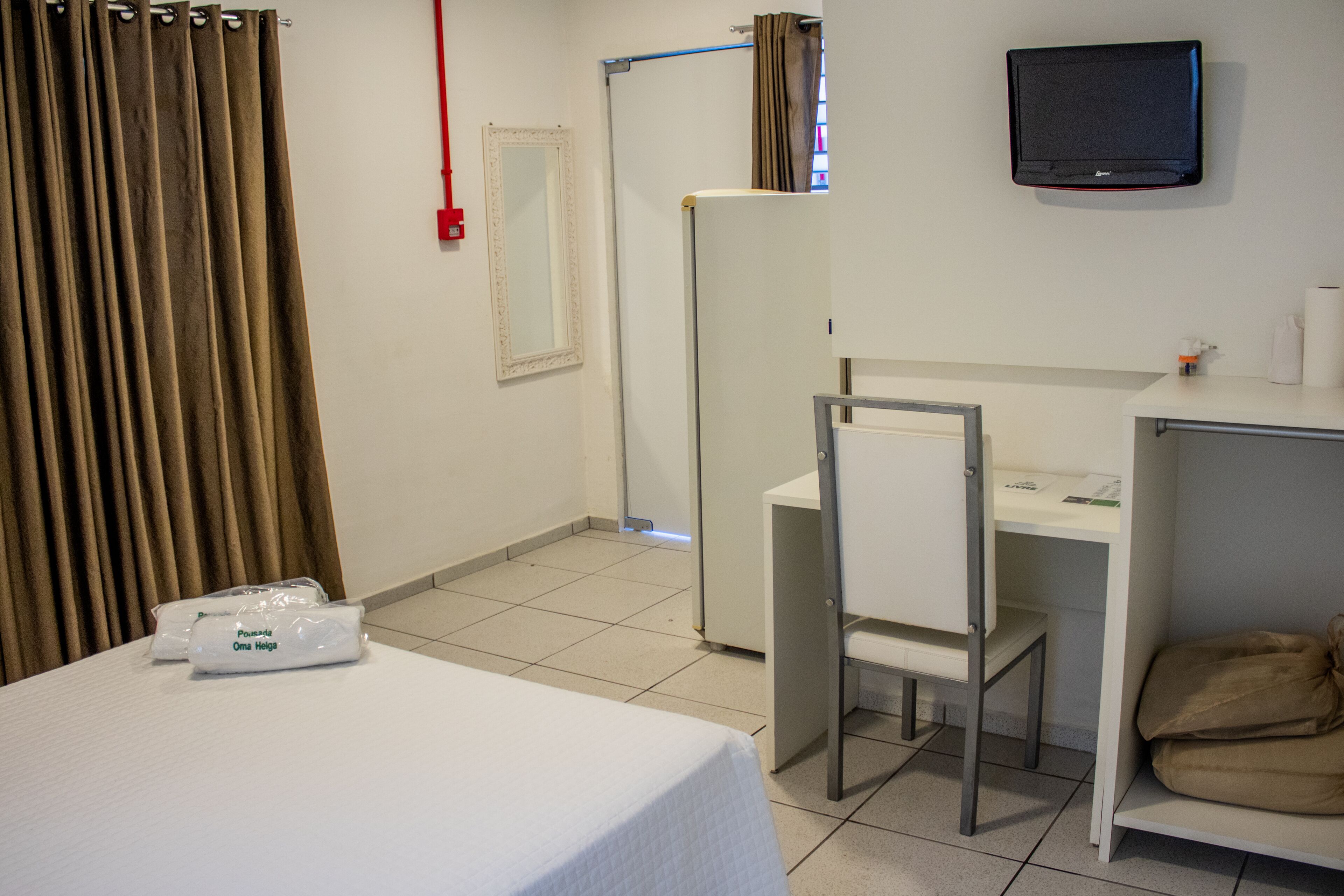Ett hotellrum med en säng, ett skrivbord, en stol, en tv och ett fönster med gardiner.