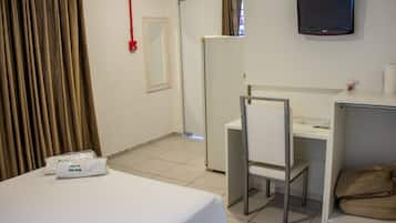 Quarto de hotel com cama, escrivaninha, cadeira, televisão e janela com cortinas.