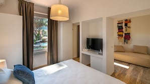 A hotel room with a bed, a TV, a sofa, and a view of an outdoor pool. - Marina Garden Hotel (Marciana Marina)
