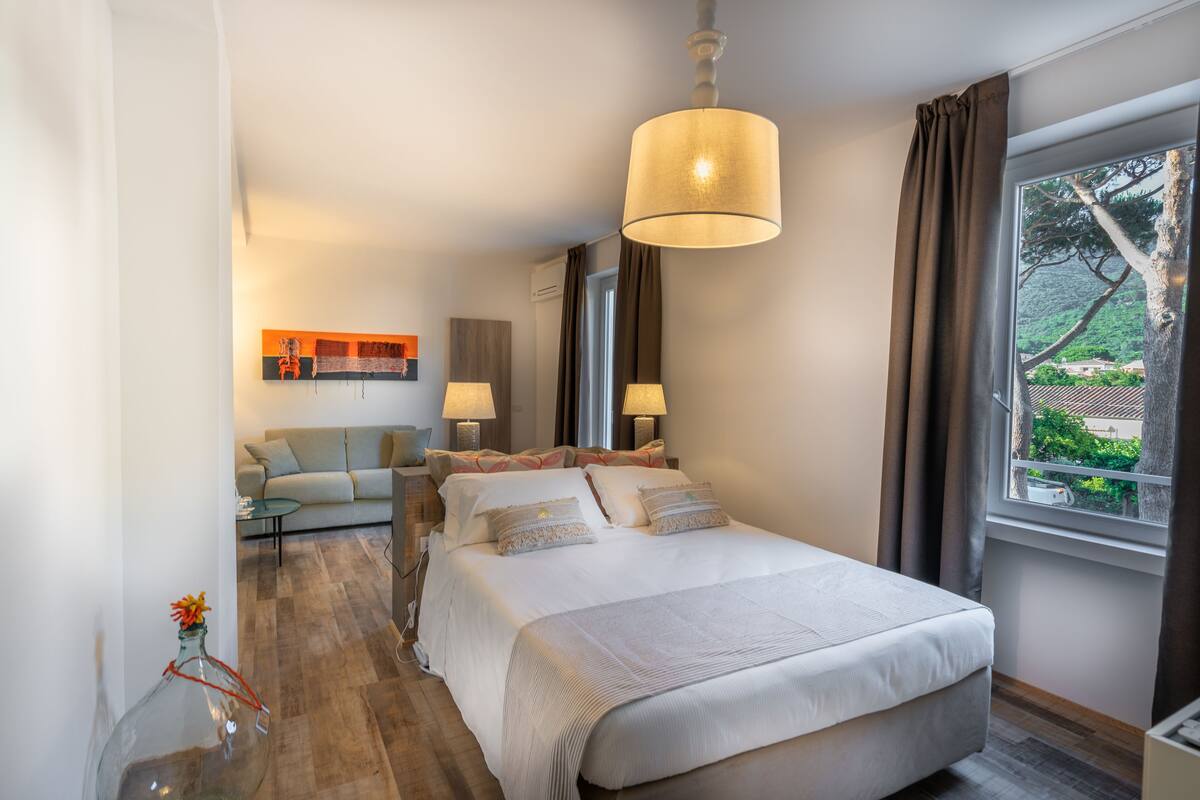 Une chambre d’hôtel moderne avec un grand lit, un canapé, une petite table et une vue sur la verdure.