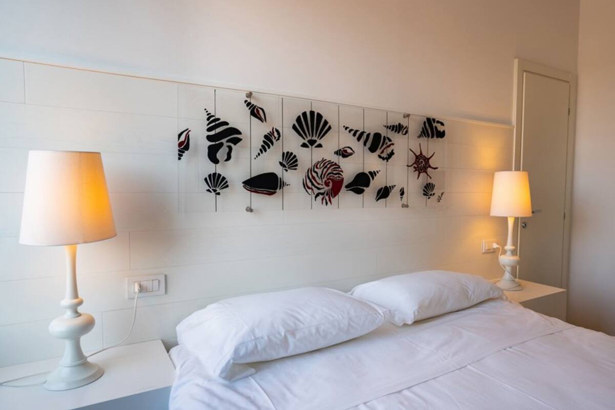 Une chambre d’hôtel avec un lit, deux lampes de chevet et un mur orné d’une œuvre d’art sur le thème de la mer.