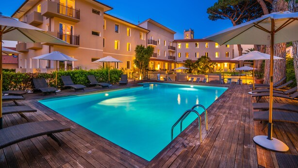 A swimming pool with lounge chairs and umbrellas, surrounded by a wooden deck and a building with balconies. - Marina Garden Hotel (Marciana Marina)