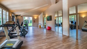 A spacious gym with exercise equipment, large windows, and a wooden floor. - Marina Garden Hotel (Marciana Marina)
