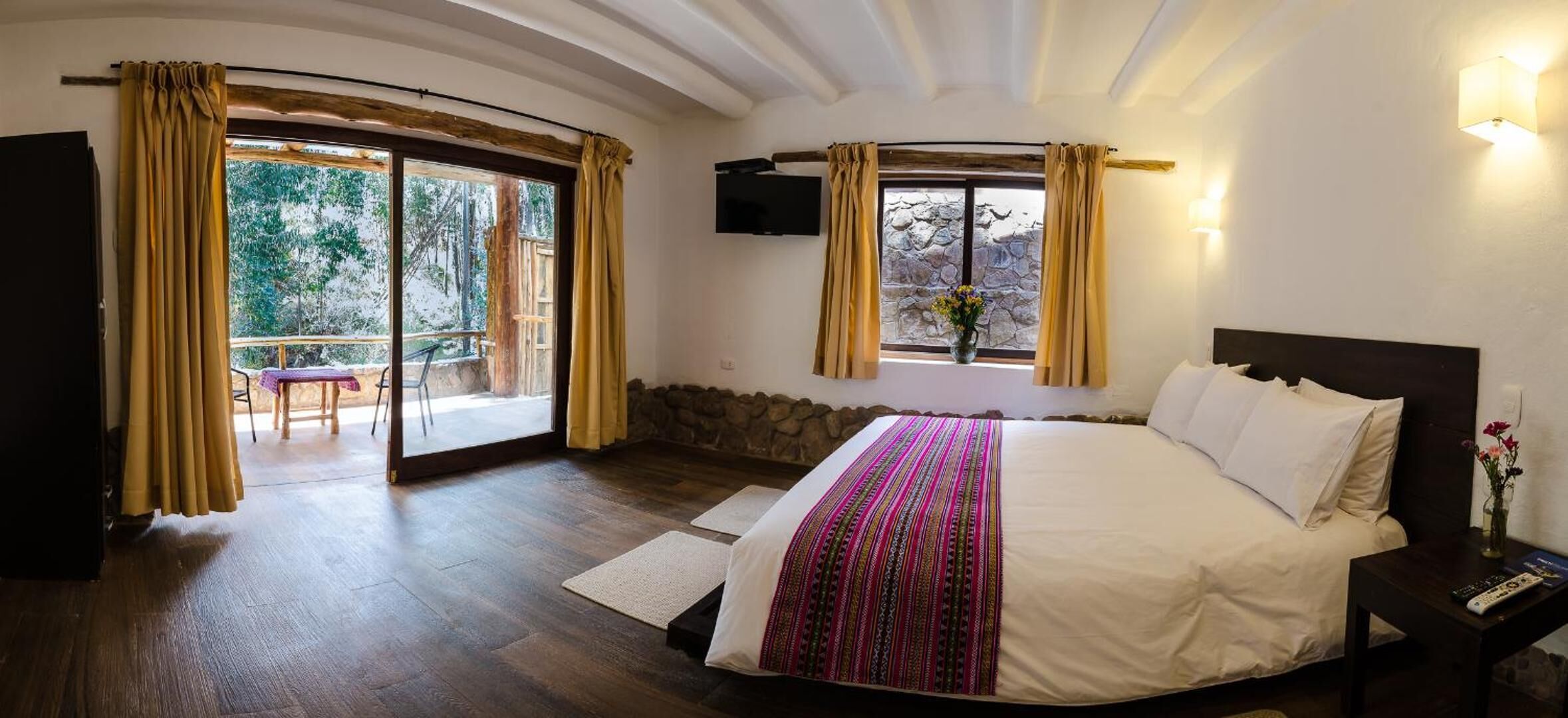 Un dormitorio con una cama grande, un televisor montado en la pared y un balcón con cortinas.