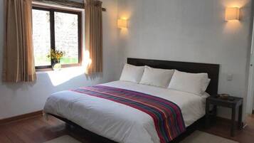A bedroom with a bed, two bedside tables, a window with curtains, and a wall-mounted light fixture.