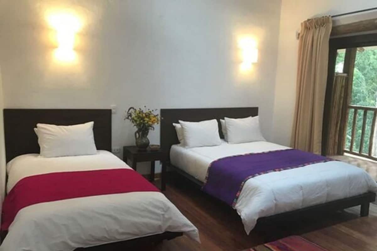 A hotel room with two beds, a nightstand with a vase of flowers, and a view through a window.