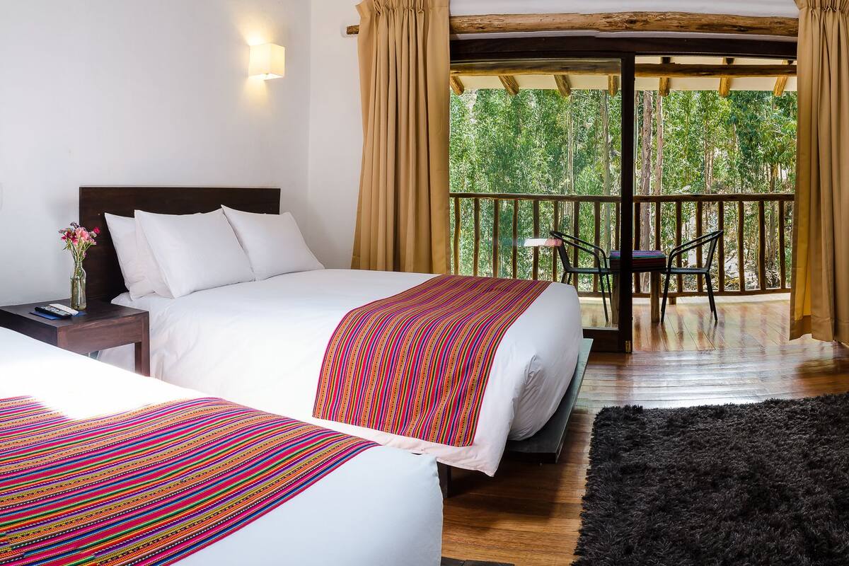 A hotel room with two beds, a balcony with a table and chairs, and a large wardrobe.