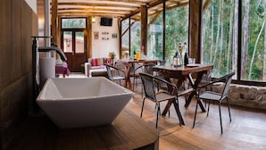 Un interior rústico de madera con un lavabo blanco grande, mobiliario de madera y vistas a la vegetación a través de ventanas amplias.