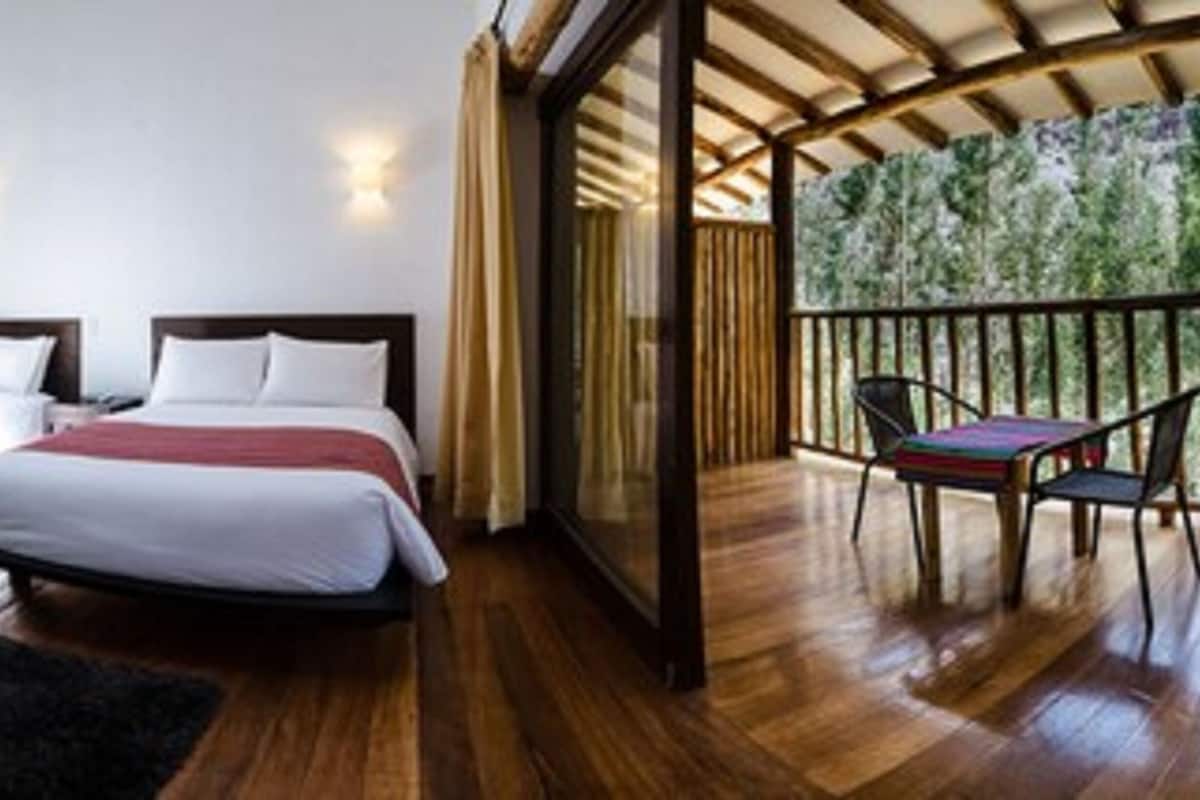 A bedroom with two beds, a black rug, and a balcony with a chair.