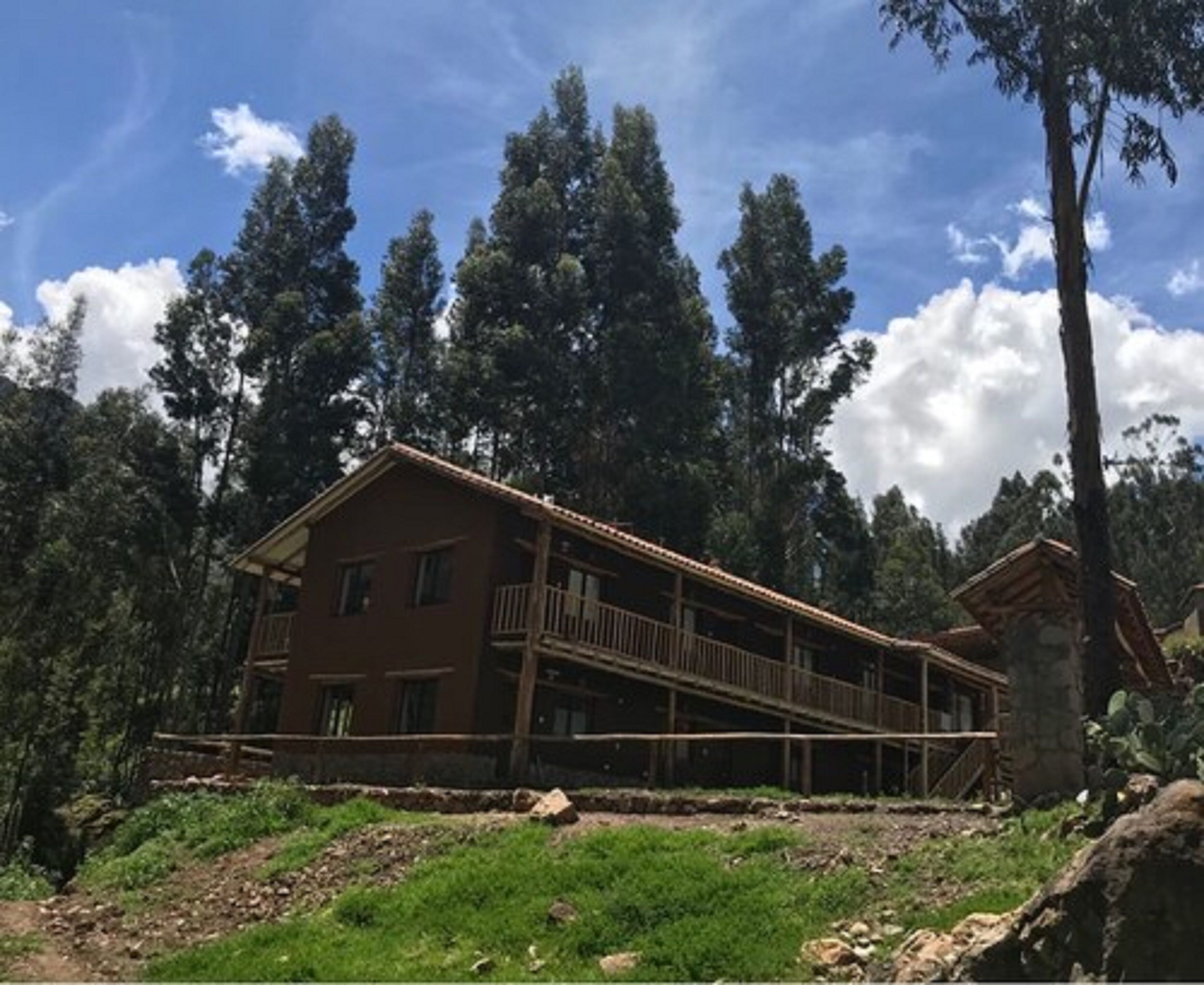 A two-story wooden building with a balcony, surrounded by trees and a clear sky.
