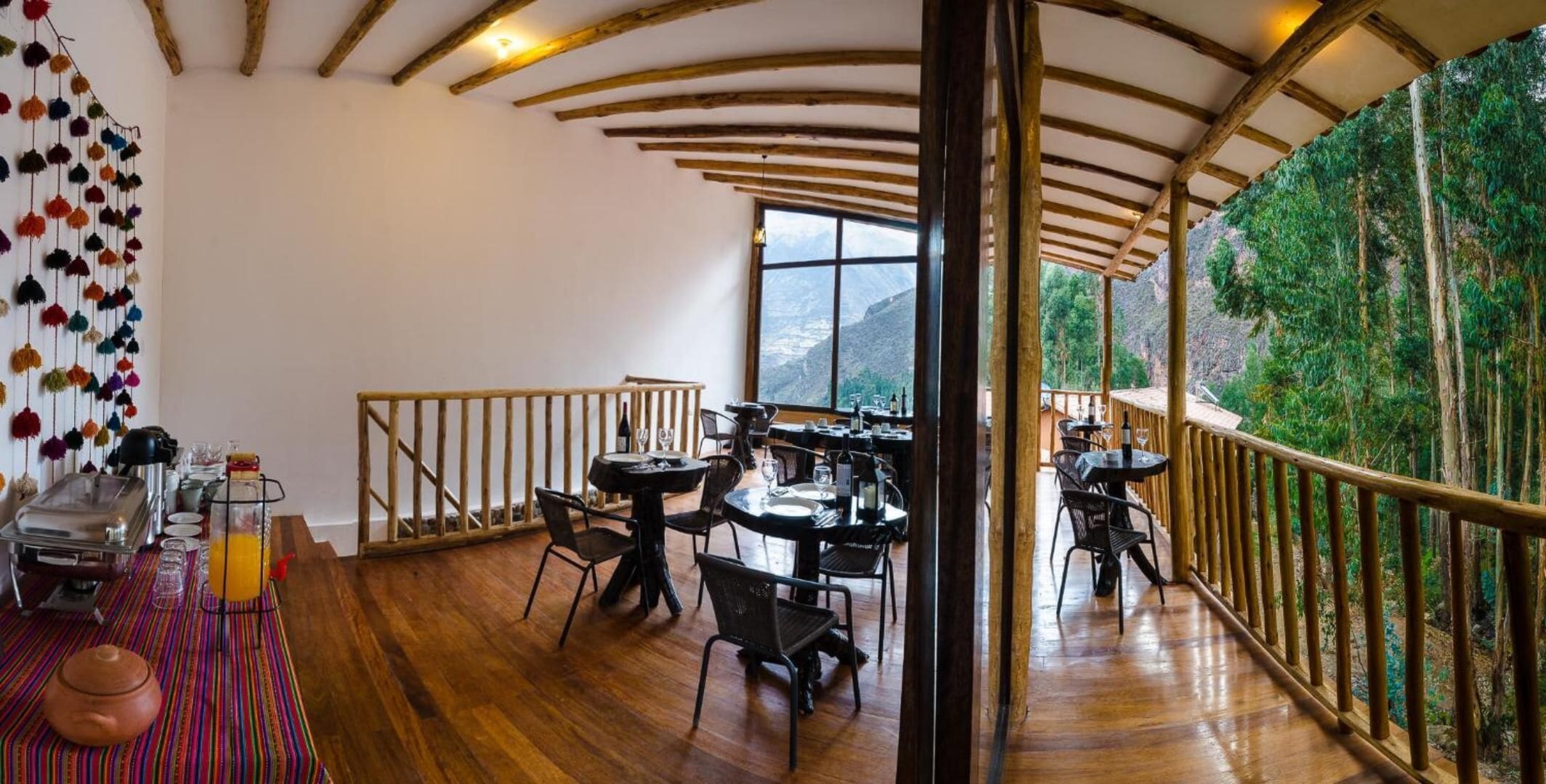 A dining area with wooden tables and chairs, a buffet setup, and a view of a mountainous landscape through large windows.