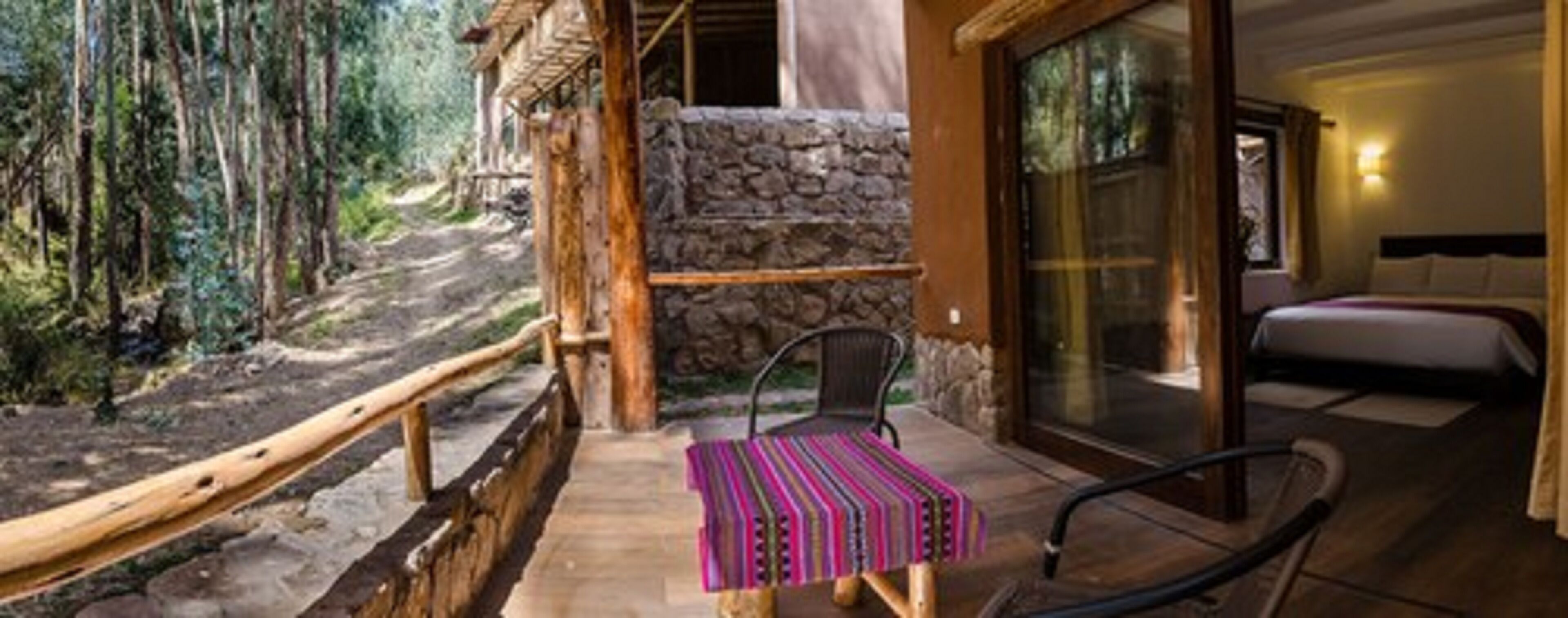 A wooden deck with a stone wall, a chair, and a bed with a view of trees.