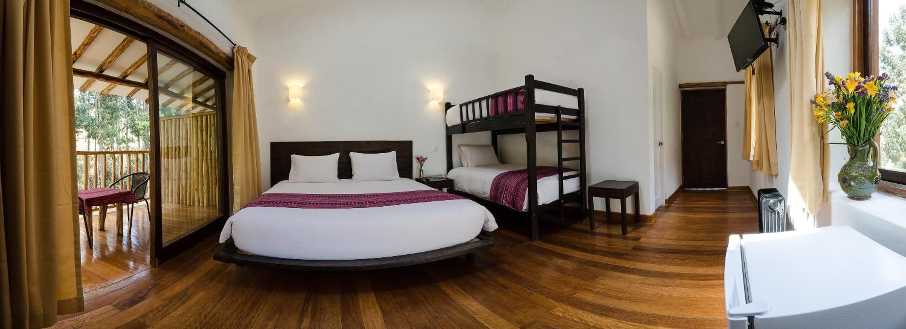 Une chambre avec un grand lit, un lit superposé, un plancher en bois, une petite table et une fenêtre avec des rideaux.
