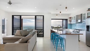 A modern kitchen with a large island, bar stools, and a view of the sea. - Island Views - the perfect holiday home. Centre of Airlie Beach. (Airlie Beach)