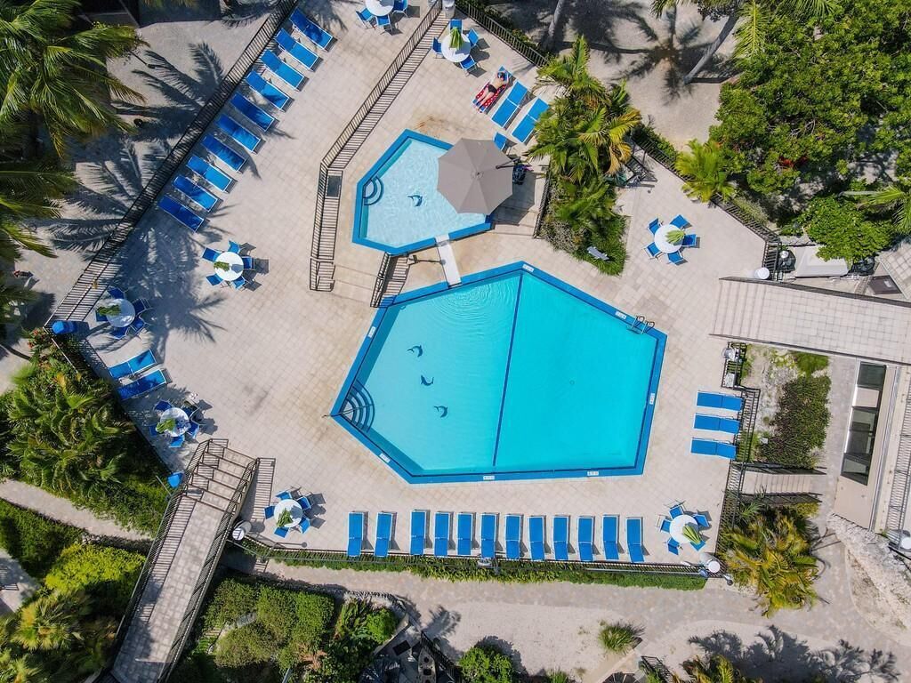 An aerial view of a pool area with multiple swimming pools, sun loungers, and palm trees.