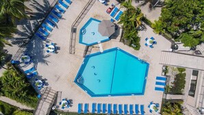 Vista aerea di una zona piscina con diverse piscine, lettini e palme.
