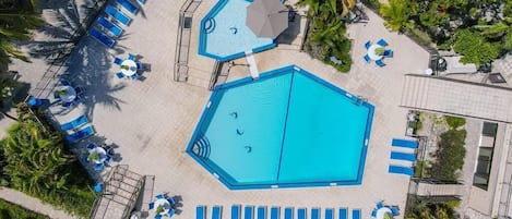 An aerial view of a pool area with multiple swimming pools, sun loungers, and palm trees.